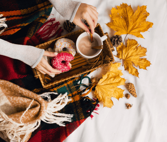 Image de mains de femmes, deux donuts, un chocolat chaud, de la cenelle, des feuilles d'automne, un plaid représentant la collection de faux ongles réutilisables d'automne