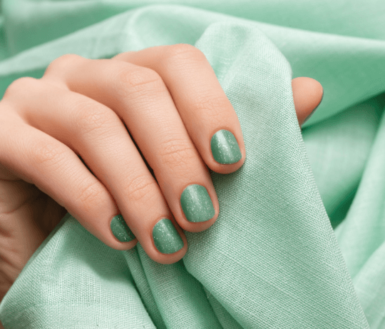 Manucure verte sur une main tenant un tissu vert pastel représentant une collection de faux ongles adhésifs vert