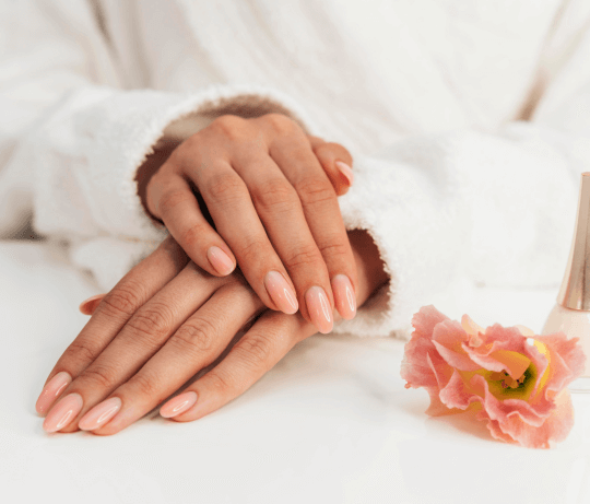 Photo d'une manucure de couleur nude avec une fleur à côté, elle représente la collection de faux ongles sans colle nude