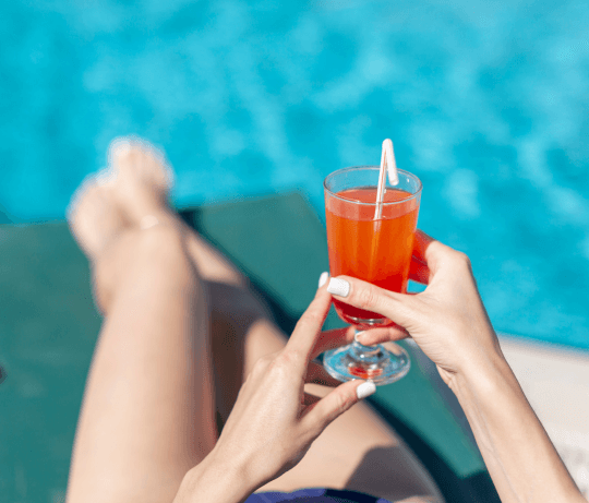 une femme portant des faux ongles réutilisable d'été sur un transat au bord d'une piscine avec un cocktail