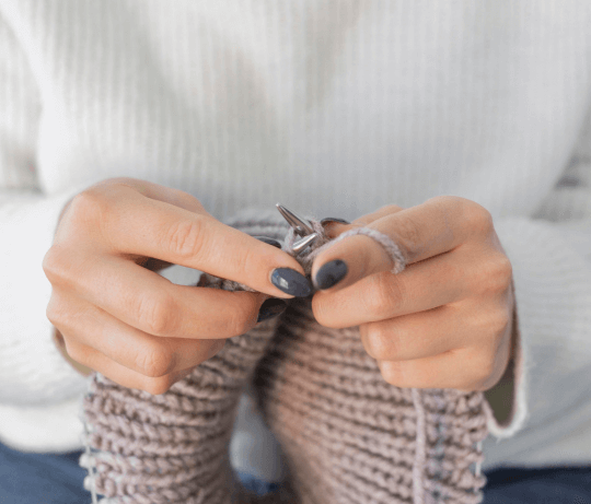 Femme tricotant une laine avec une manucure grise, représentant la collection de faux ongles sans colle gris