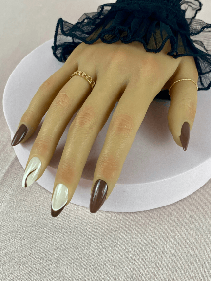 Mains portant des faux ongles réutilisables sans colle de couleurs marron avec un premier nail art qui a deux lignes, une blanche et une marron puis le deuxième nail art à une French manucure marron avec une ligne blanche. 