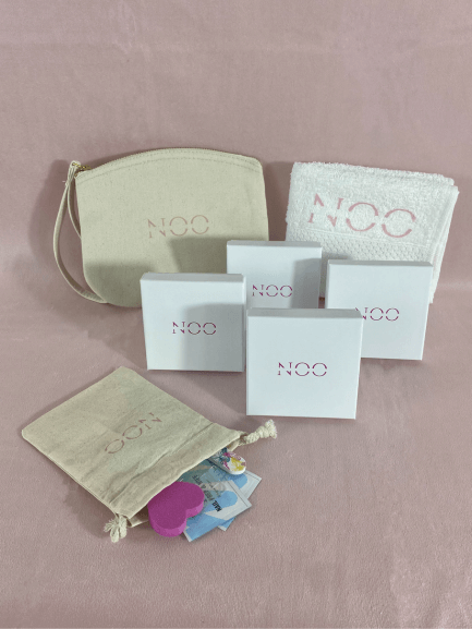 Une pochette de la marque NailsOnOff, une serviette NailsOnOff, quatre boîtes de kit de faux ongles avec son pochon d'accessoires pour limes à ongles, bloc polissoir, repousse cuticule sur fond rose