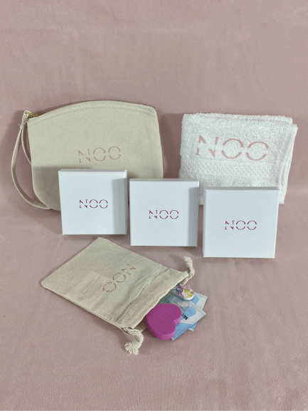 Une pochette de la marque NailsOnOff, une serviette NailsOnOff, trois boîtes de kit de faux ongles avec son pochon d'accessoires pour limes à ongles, bloc polissoir, repousse cuticule sur fond rose