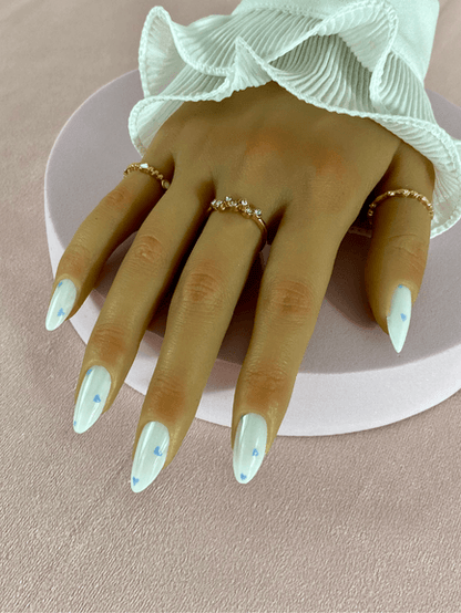 Kit de faux ongles réutilisables à coller à l'aide d'adhésifs avec des designs variés, incluant des petits coeurs bleu clair, couleur principale blanc, en forme d'amande.