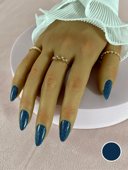 Faux ongles réutilisables à coller avec des adhésifs, couleur bleu foncé à paillette, en forme amande et finition brillante.